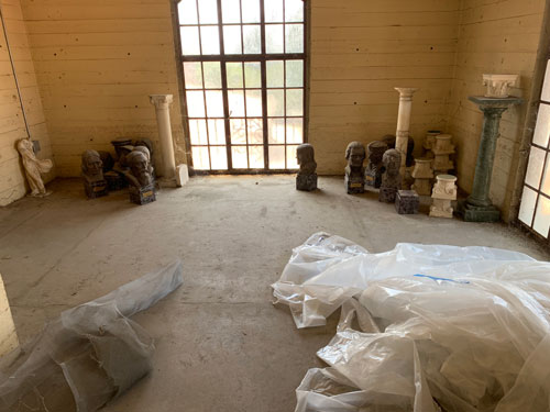[View further down the hallway of
concrete room lit by large windows with columns, busts, and a pile of plastic
tarp on the floor.]