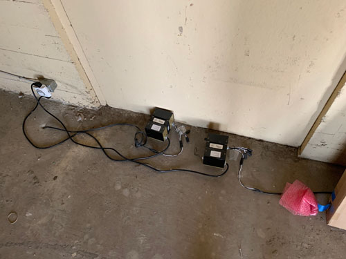 [Concrete floor lined with
various black boxes with wires going in and out, some going through the floor,
some plugged into a nearby outlet.]