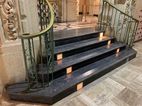 [Elaborate metal balustrade
flanks a polished black stone staircase with built-in lights that leads up to a
floor of inlaid marble.]