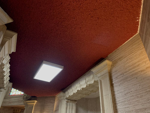 [Elaborate archways through stone
walls lead into and out of a corridor with an out-of-place dark red spray-on
"popcorn" ceiling and a large boxy light fixture.]