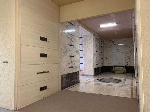 [A corridor connects two parts of
the mausoleum decorated in contrasting styles: On the near side, carpet and
plain stone walls; on the far side, elaborately inlaid marble walls and floors,
all lined with graves.]