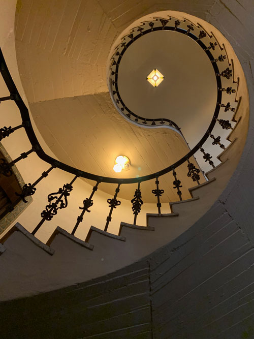 [View up a spiraling concrete
staircase with an elaborate iron balustrade.]
