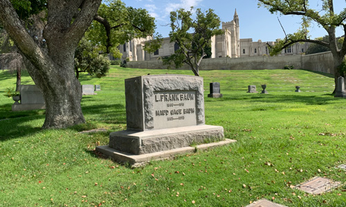 [View of an upright gravestone on a
green hill bearing the name "L. Frank Baum" with a large Italianate building in
the background.]