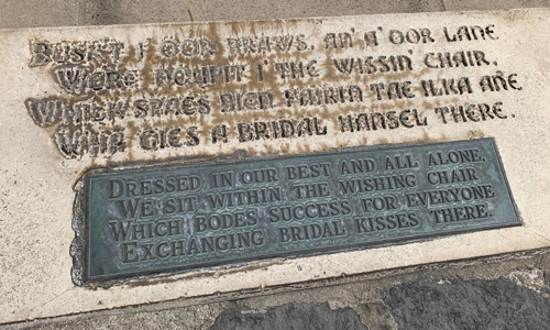 [Cut stone and copper signs set
into the pavement below "the Wishing Chair," transcribed below.]