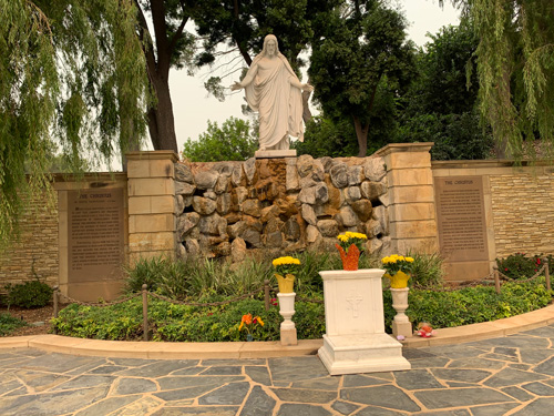 [Another, larger "Christus"
statue, mounted over a fountain in the form of a trickle of water over a wall of
boulders; facing the statue across a small garden, a low marble alter made for
kneeling on.]