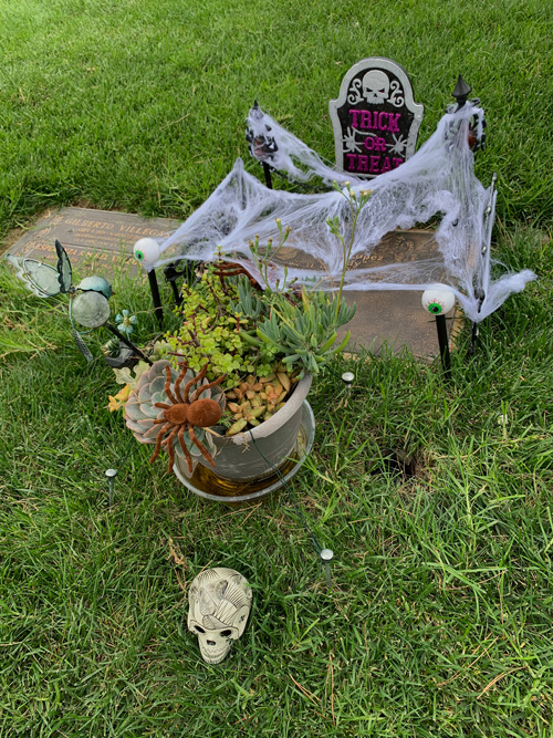 [Copper grave marker decorated
with fake cobwebs, a planter full of succulents, a plastic skull, and a small
plastic sign in the shape of an upright grave bearing the image of a skull and
the words "Trick or treat."]