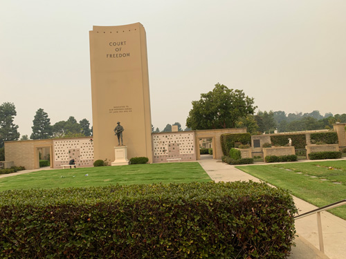 [View of a distant bronze
sculpture on a pedestal below a tall structure that serves as a sign announcing
the "Court of Freedom"; the walls flanking this tower are covered with small
graves, probably marking where ashes are interred.]