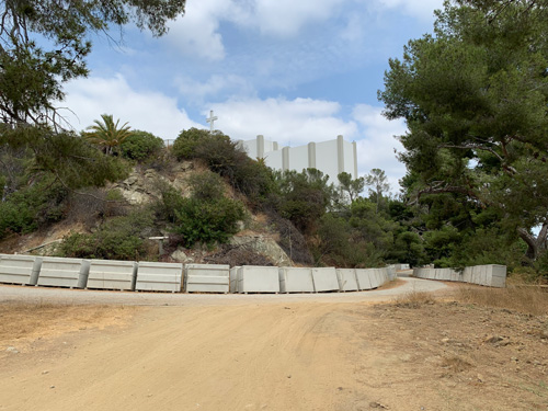 [View from a dirt road of
concrete vaults and the same hill, beyond which is a large, windowless building
with a large cross on top.]