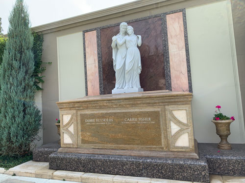[Sarcophagus in multiple kinds
of stone topped with a marble statue of one robed figure leaning against
another; engraved on the front are the names "Debbie Reynolds" and "Carrie
Fisher.".]
