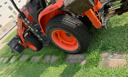 [Closer look of a bright orange
backhoe parked on a row of graves.]