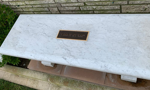 [Marble bench with a metal sign
set inside bearing a brief message, transcribed below.]