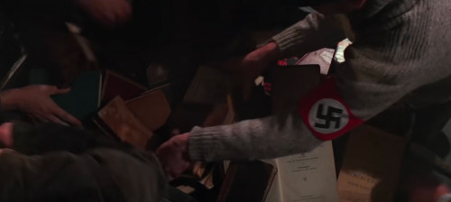[Still from the Nazi
book-burning rally scene in the film "Indiana Jones and the Last Crusade": Many
arms reach into a pile of books to throw onto the fire; one sleeve displays a
prominent swastika.]