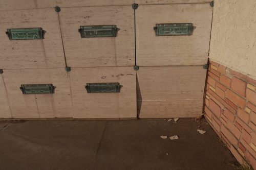[Wall with metal lettering
announcing the "Sanctuary of Peaceful Repose" containing a courtyard with a
bright green lawn full of graves on which can be seen, under a solitary tree, a
small, orange backhoe.]